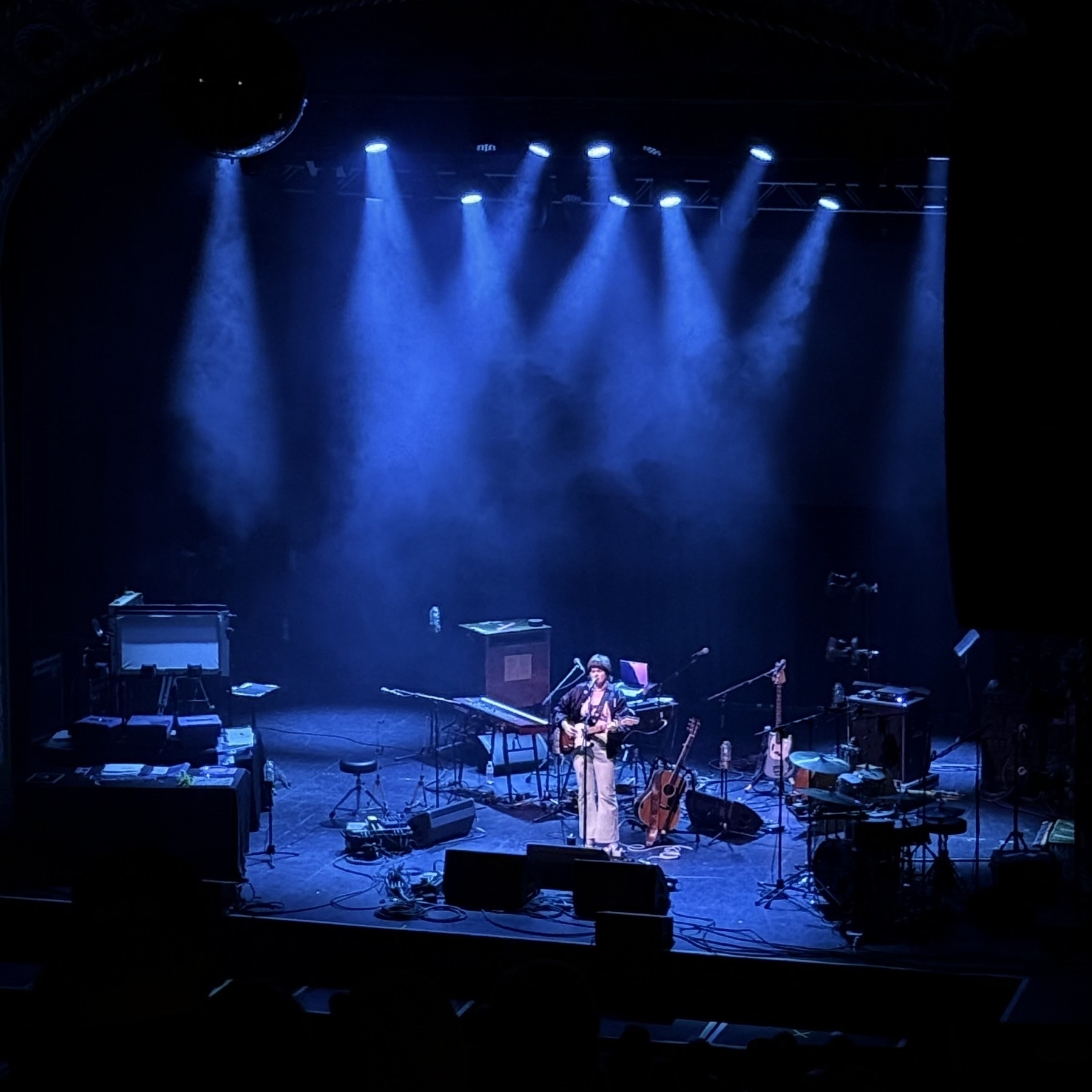 Auto-generated description: A person is performing on a dimly lit stage with various musical instruments and equipment scattered around.
